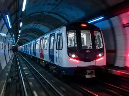 Ein moderner Londoner U-Bahn-Zug fährt schnell durch einen Tunnel, mit blauen und roten Lichtakzenten. - Foto: über boerse-global.de
