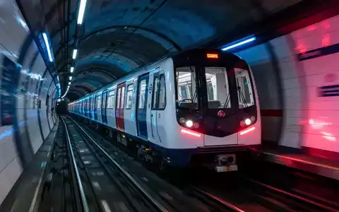 Ein moderner Londoner U-Bahn-Zug fährt schnell durch einen Tunnel, mit blauen und roten Lichtakzenten. - Foto: über boerse-global.de