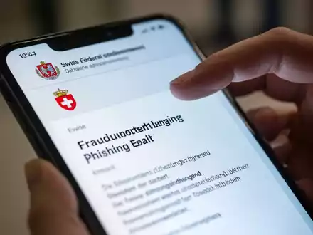 Nahaufnahme eines Smartphones mit einer gefälschten Phishing-E-Mail, die ein Schweizer Regierungslogo zeigt, und einer darüber schwebenden Hand. - Foto: über boerse-global.de
