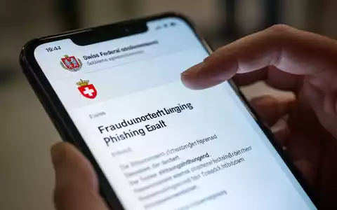 Nahaufnahme eines Smartphones mit einer gefälschten Phishing-E-Mail, die ein Schweizer Regierungslogo zeigt, und einer darüber schwebenden Hand. - Foto: über boerse-global.de