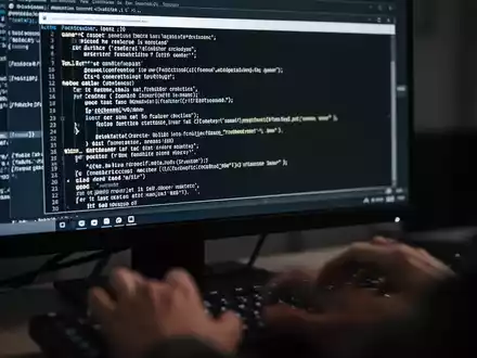 Close-up of a computer screen showing code in a command prompt, with hands typing on a keyboard blurred in the foreground. - Foto: über boerse-global.de