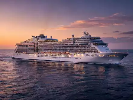 Ein luxuriöses Kreuzfahrtschiff, 'Mein Schiff Flow', segelt bei Sonnenuntergang auf einem ruhigen blauen Meer. - Foto: über boerse-global.de