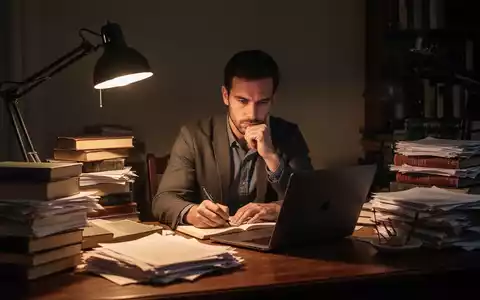 Ein einsamer Schriftsteller sitzt an einem Schreibtisch, umgeben von Büchern und Papieren, während er über sein Manuskript nachdenkt. - Foto: über boerse-global.de