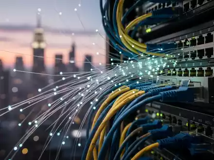 Close-up of fiber optic cables and network hardware with a blurred city skyline at dusk in the background, symbolizing digital infrastructure. - Foto: über boerse-global.de