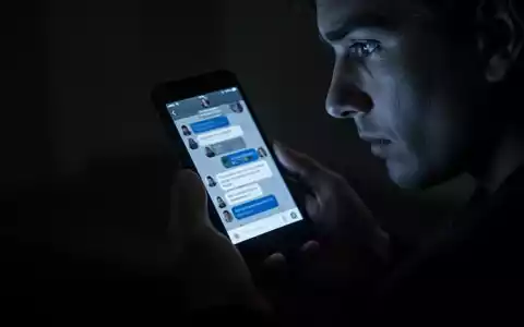 A person's hands holding a smartphone, its screen casting a dim glow on their face, reflecting a chat interface. - Foto: über boerse-global.de