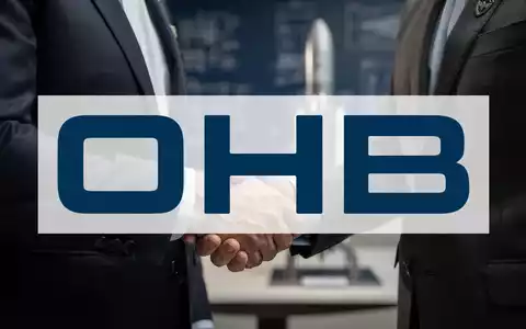 Nahaufnahme eines Händedrucks zwischen zwei Anzugträgern vor einem verschwommenen Hintergrund mit Bauplänen und einem Raketenmodell. - Foto: über boerse-global.de