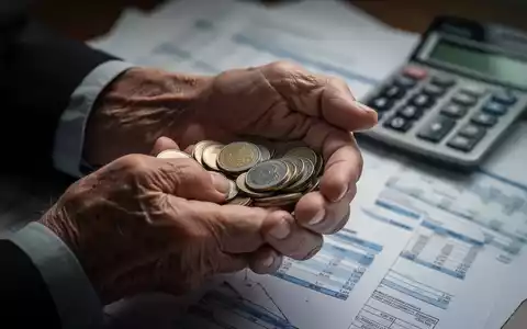 Ältere Hände halten Münzen, im Hintergrund verschwommen Finanzdokumente und ein Taschenrechner. Symbolisiert steigende Rentenbeiträge. - Foto: über boerse-global.de