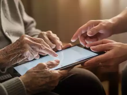 Ältere Hände benutzen ein Tablet, eine jüngere Hand führt sie, symbolisiert digitale Bildung und generationenübergreifende Unterstützung. - Foto: über boerse-global.de