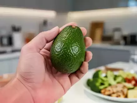 Nahaufnahme einer Hand, die eine reife Avocado hält, mit einem unscharfen Hintergrund, der eine gesunde Mahlzeit oder Küche andeutet. - Foto: über boerse-global.de
