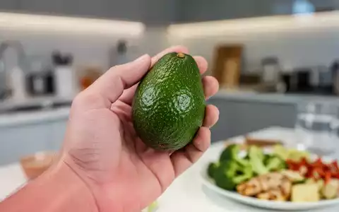 Nahaufnahme einer Hand, die eine reife Avocado hält, mit einem unscharfen Hintergrund, der eine gesunde Mahlzeit oder Küche andeutet. - Foto: über boerse-global.de