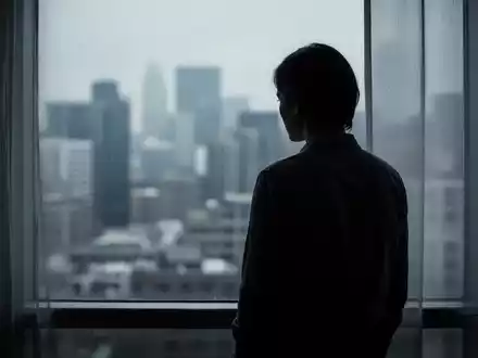 Eine nachdenkliche Silhouette einer Person, die vor einem Fenster steht und auf eine unscharfe Stadt blickt. - Foto: über boerse-global.de