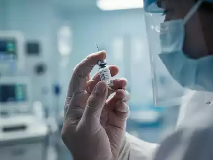 Nahaufnahme einer Hand, die eine Spritze oder ein medizinisches Fläschchen hält, mit unscharfem medizinischem Hintergrund. - Foto: über boerse-global.de