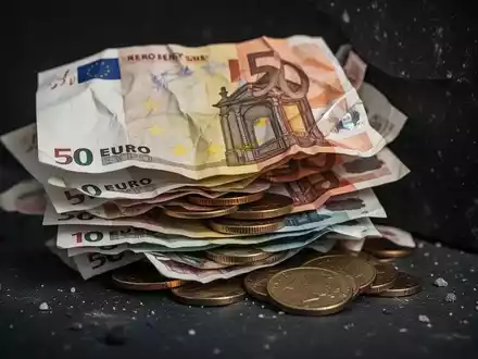Ein Nahaufnahme-Bild von zerknüllten deutschen Euro-Banknoten und Münzen, die auf einer dunklen Oberfläche liegen und finanzielle Not andeuten. - Foto: über boerse-global.de