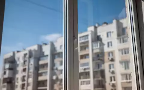Nahaufnahme eines modernen, energieeffizienten Fensters, das einen blauen Himmel reflektiert, mit einem Wohngebäude im Hintergrund. - Foto: über boerse-global.de