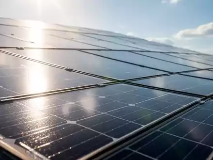 Nahaufnahme einer Solaranlage, die einen hellen Himmel widerspiegelt, mit Sonnenstrahlen, die auf die Zellen treffen. - Foto: über boerse-global.de