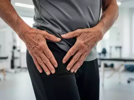 Eine ältere Person berührt sanft ihre Hüfte während einer Dehnübung in einem hellen Physiotherapie-Studio. - Foto: über boerse-global.de