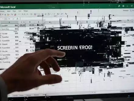 Eine Hand interagiert mit einer verzerrten, glitchenden Microsoft Excel-Tabelle auf einem Computerbildschirm, der fehlerhafte Daten anzeigt. - Foto: über boerse-global.de