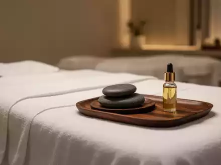 Ein ruhiger Massageraum mit einem Massagetisch, weißen Laken, einem heißen Stein und einer Flasche ätherisches Öl. - Foto: über boerse-global.de