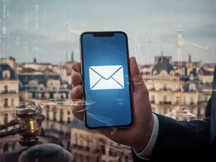 Hand holding a smartphone displaying an email icon, with a subtle overlay of legal scales, against a digital and cityscape background. - Foto: über boerse-global.de