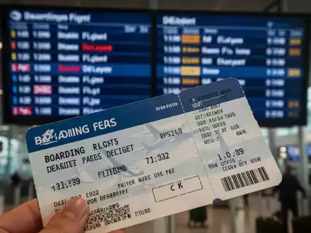 Eine Nahaufnahme einer Bordkarte mit einem unscharfen Anzeigebildschirm am Flughafen, der Flugverspätungen anzeigt. - Foto: über boerse-global.de