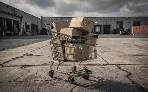 Ein leicht verbeulter Einkaufswagen, überfüllt mit Kartons, wirft einen langen Schatten unter einem trüben Himmel. - Foto: über boerse-global.de