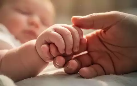 Eine Nahaufnahme einer Babyhand, die sanft einen Erwachsenenfinger hält, symbolisiert Bindung und Zärtlichkeit. - Foto: über boerse-global.de