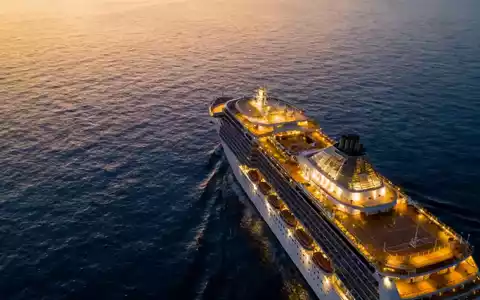 Ein luxuriöses Kreuzfahrtschiff bei Sonnenuntergang auf ruhigem blauen Meer, beleuchtet, symbolisiert Freizeit und Reisen. - Foto: über boerse-global.de