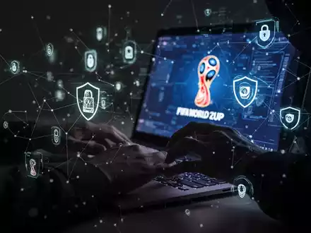 A shadowy figure's hands typing on a laptop, with security icons and network lines, symbolizing online fraud during the FIFA World Cup. - Foto: über boerse-global.de