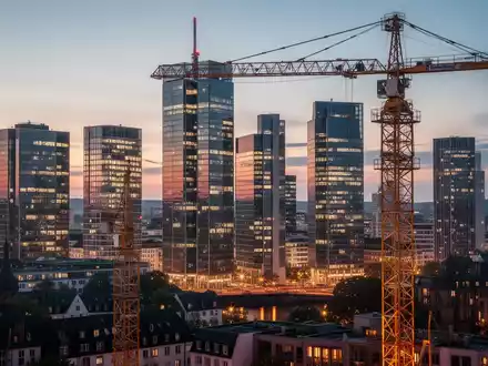 Frankfurter Skyline bei Sonnenuntergang mit modernen Bürogebäuden und einem Baukran, der den Fortschritt der Stadtentwicklung symbolisiert. - Foto: über boerse-global.de