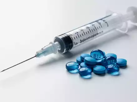 Eine medizinische Spritze liegt neben einem kleinen Haufen blauer Vitamin-B12-Pillen auf einer sterilen weißen Oberfläche. - Foto: über boerse-global.de