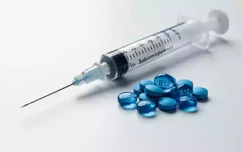 Eine medizinische Spritze liegt neben einem kleinen Haufen blauer Vitamin-B12-Pillen auf einer sterilen weißen Oberfläche. - Foto: über boerse-global.de