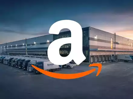 Ein riesiges, modernes Amazon-Logistikzentrum bei Sonnenaufgang mit vielen Lieferwagen, die aufgereiht sind. - Foto: über boerse-global.de