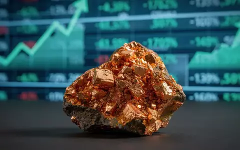 Ein glänzendes Kupfererzstück im Vordergrund, unscharfer Hintergrund mit einem Aktien-Ticker, der positive Trends zeigt. - Foto: über boerse-global.de