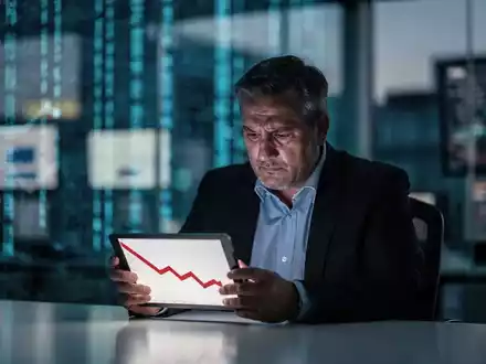 Ein nachdenklicher Geschäftsmann betrachtet ein Tablet mit einem fallenden Aktienkursdiagramm in einem modernen Büro. - Foto: über boerse-global.de