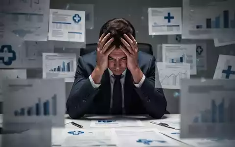 Eine Person sitzt am Schreibtisch mit dem Kopf in den Händen, umgeben von verschwommenen Finanzdokumenten und medizinischen Symbolen. - Foto: über boerse-global.de