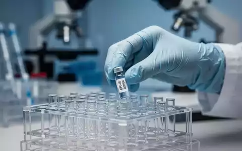 Nahaufnahme einer behandschuhten Hand, die ein kleines Reagenzglas mit der Aufschrift 'ER-100' in ein Laborregal stellt. - Foto: über boerse-global.de