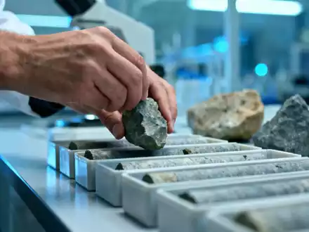 Geologenplatzierung von Gesteinskernproben in Behältern in einem Labor mit wissenschaftlicher Ausrüstung im Hintergrund. - Foto: über boerse-global.de