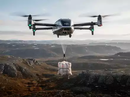 An autonomous Pyka DropShip cargo drone flying over a remote landscape, releasing a package via parachute. - Foto: über boerse-global.de