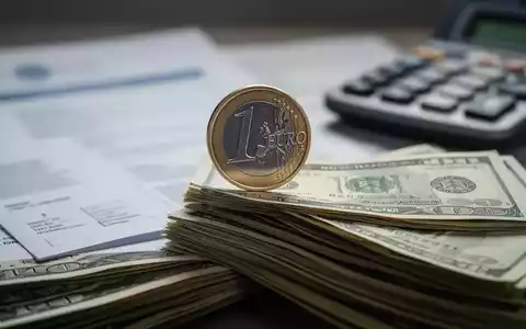 Eine einzelne Euromünze balanciert auf einem Stapel Geldscheine, im Hintergrund unscharfe Dokumente und ein Taschenrechner. - Foto: über boerse-global.de
