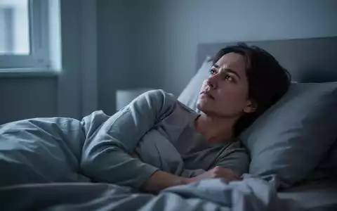 Eine Person liegt wach und nachdenklich im Bett, umgeben von kühlem Umgebungslicht, das durch ein Fenster fällt. - Foto: über boerse-global.de