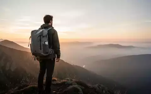 Ein einsamer Wanderer mit minimalistischem Rucksack auf einem Bergrücken bei Sonnenaufgang, der über eine weite, neblige Landschaft blickt. - Foto: über boerse-global.de