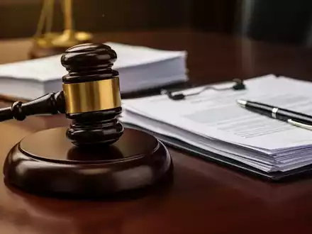 Ein Nahaufnahme eines Holzhammers auf einem dunklen Schreibtisch, umgeben von juristischen Dokumenten und einem Stift. - Foto: über boerse-global.de