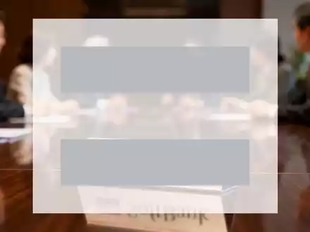 Ein eleganter Konferenztisch mit einem stilisierten SoftBank-Logo auf einem Namensschild, unscharf im Hintergrund diskutierende Führungskräfte. - Foto: über boerse-global.de