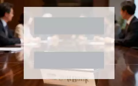 Ein eleganter Konferenztisch mit einem stilisierten SoftBank-Logo auf einem Namensschild, unscharf im Hintergrund diskutierende Führungskräfte. - Foto: über boerse-global.de