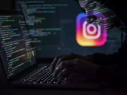 A person's hands typing on a laptop keyboard, with code reflecting on their face, and a blurred Instagram logo in the background. - Foto: über boerse-global.de