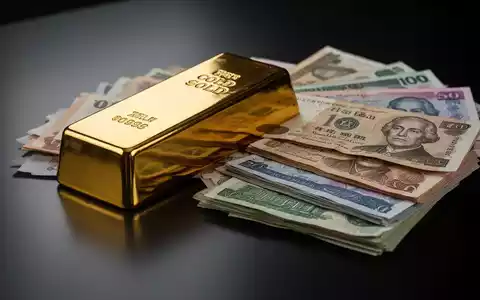 Ein glänzender Goldbarren neben einem Stapel internationaler Banknoten auf einer dunklen Oberfläche. - Foto: über boerse-global.de