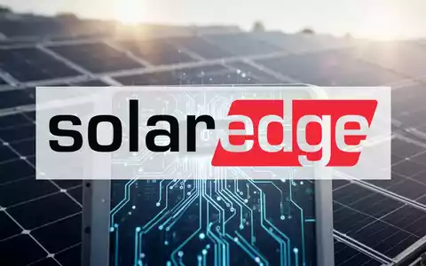 Nahaufnahme eines modernen Solar-Wechselrichters mit sichtbarer Schaltung vor einem unscharfen, sonnenbeschienenen Solarmodulfeld. - Foto: über boerse-global.de