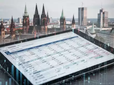Ein modernes digitales Hauptbuch oder eine Tabelle auf einem Tablet, mit verschwommenen Elementen einer deutschen Stadtlandschaft im Hintergrund. - Foto: über boerse-global.de