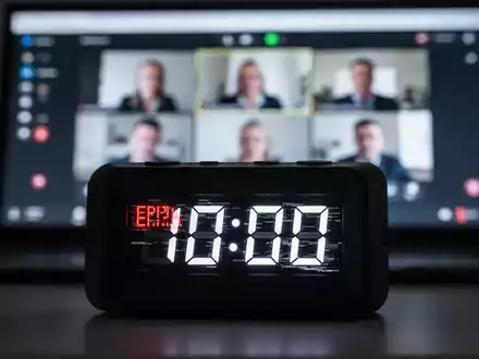 A close-up of a digital clock with a glitchy display, indicating a technical error, with a blurred video conferencing screen in the background. - Foto: über boerse-global.de