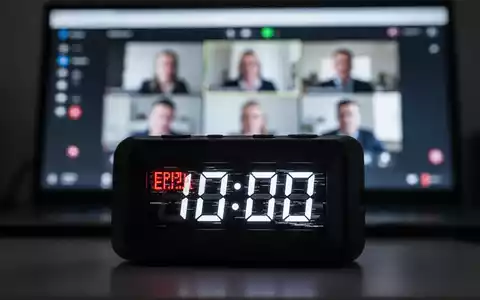 A close-up of a digital clock with a glitchy display, indicating a technical error, with a blurred video conferencing screen in the background. - Foto: über boerse-global.de